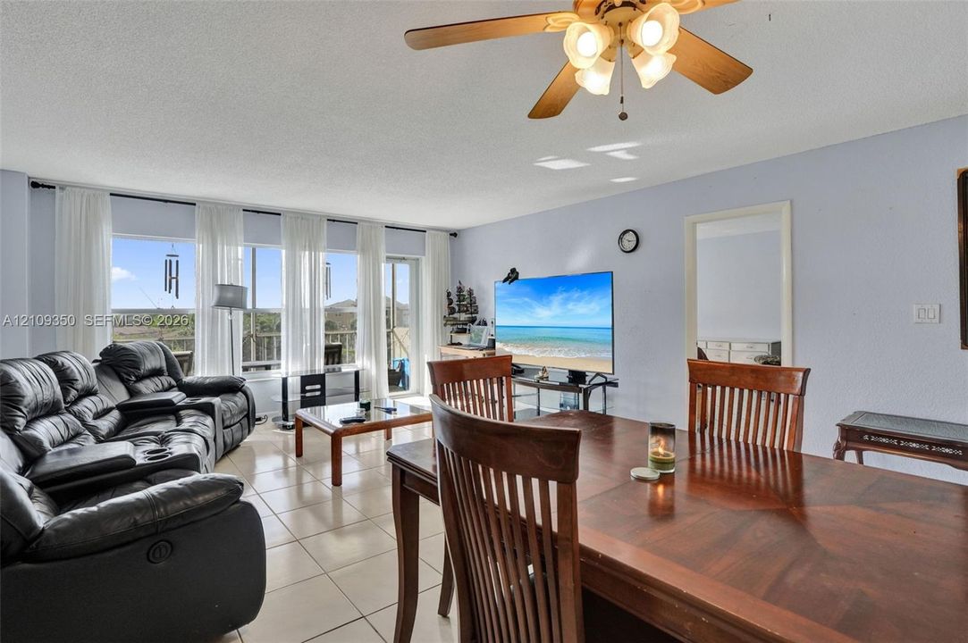 Living area featuring large-format ceramic tile flooring, a multi-light ceiling fan, and a floor-to-ceiling glass wall with access to an exterior space