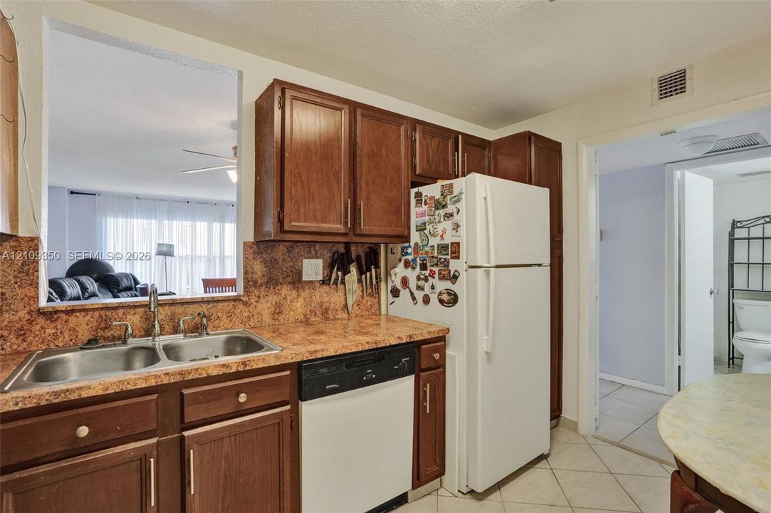 Kitchen featuring dark wood cabinetry, laminate countertops with a stone-finish pattern, a double-basin stainless steel sink, and a built-in dishwasher