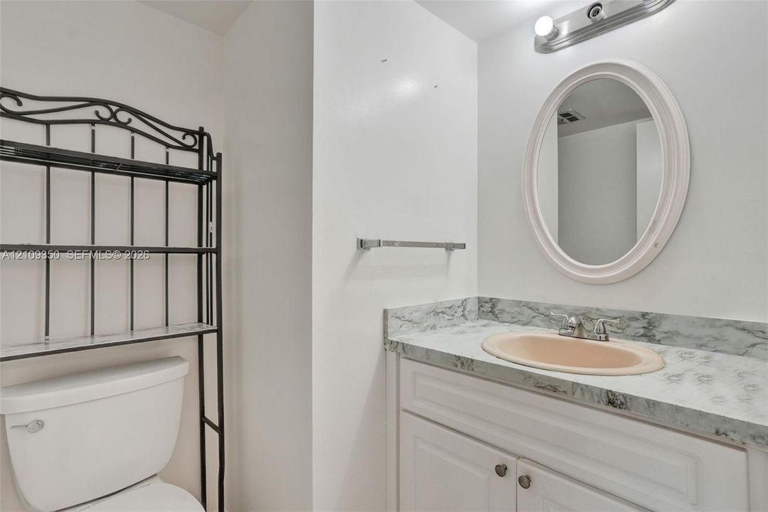 Vanity featuring a stone-patterned countertop, integrated oval sink, chrome dual-handle faucet, white cabinetry, and an oval mirror with overhead lighting