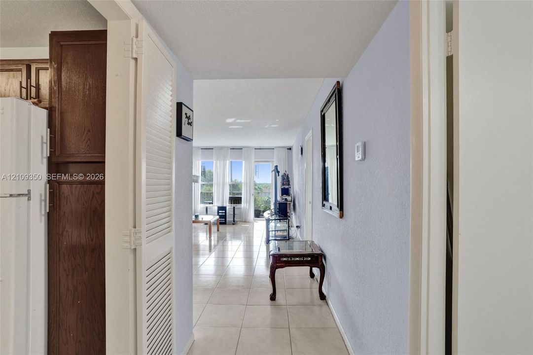 Interior hallway featuring large-format tile flooring, white louvered-door closet, and dark wood-finish cabinetry