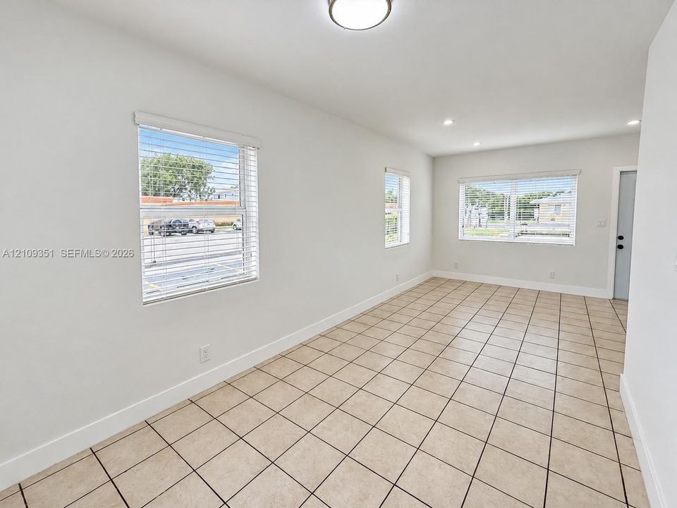 Neutral-toned tile flooring, recessed and flush-mount lighting, and large windows with horizontal blinds