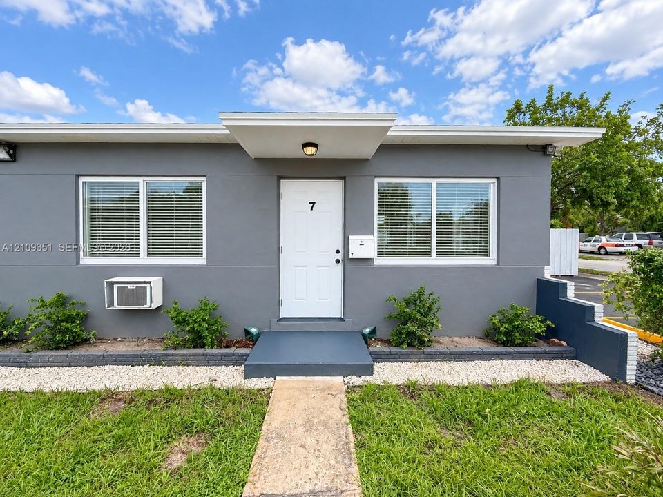 Exterior facade featuring a smooth gray finish, flat roofline with a covered entryway, dual sliding windows, and a structured concrete walkway