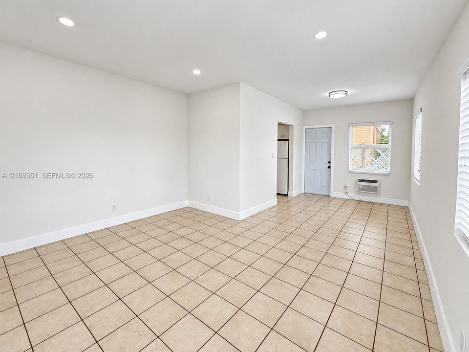 Neutral-toned tile flooring, recessed ceiling lighting, wall-mounted air conditioning unit, and large window with integrated blinds