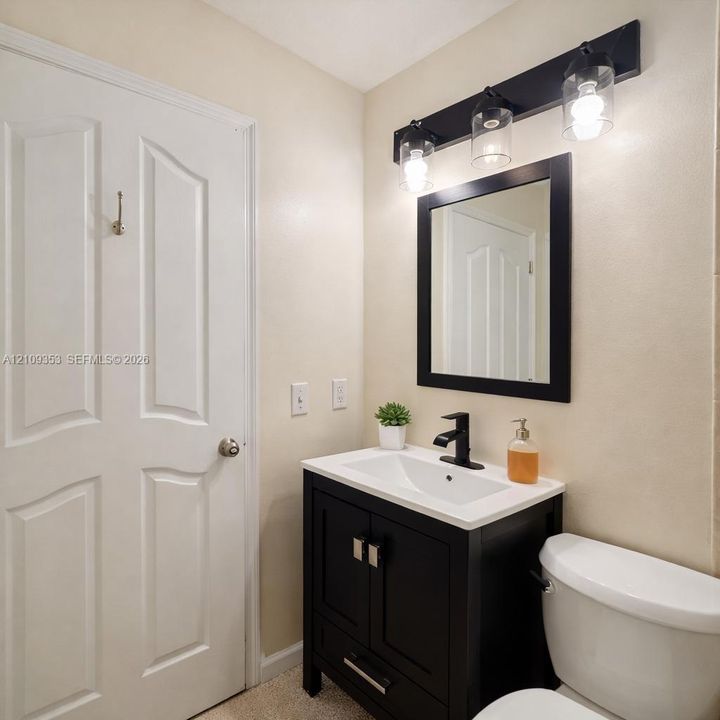 Dark-finished vanity with a white countertop and integrated sink, matte black faucet, framed mirror, and three-light wall-mounted fixture