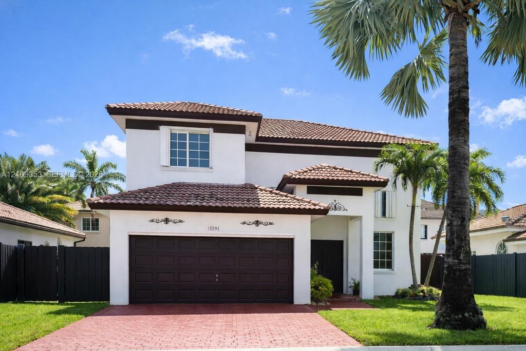 Two-story stucco exterior with a tiled roof, attached two-car garage, red paver driveway, and exterior decorative metal accents