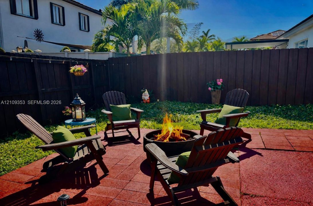 Rear patio featuring a fire pit, paved flooring, perimeter wood fencing, and mature palm trees