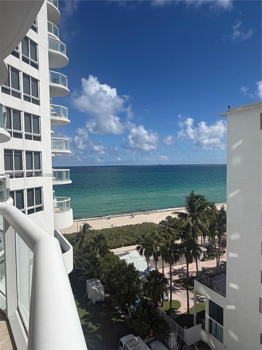 Elevated balcony featuring glass railings and direct oceanfront scenery, accompanied by high-rise architectural elements