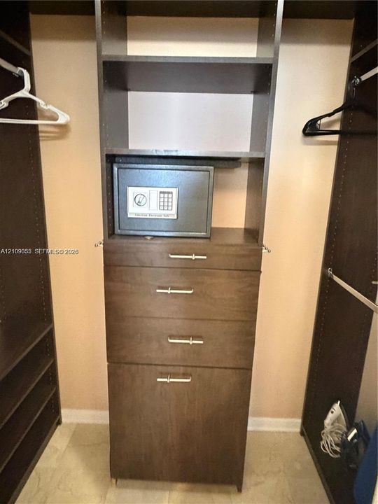Custom built-in closet organization system featuring dark wood-finish cabinetry, four integrated storage drawers, vertical shelving, and metallic hardware