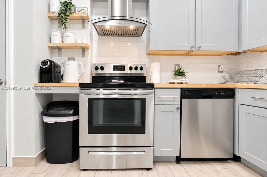 Kitchen featuring light-toned cabinetry, wood countertops, stainless steel appliances, a subway tile backsplash, and wall-mounted shelving