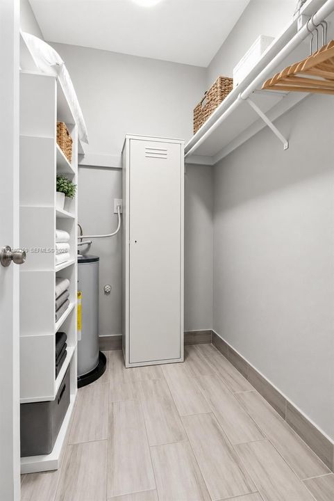 Storage space featuring built-in white shelving, a full-height metal cabinet, wall-mounted hanging rod, and wood-finish tile flooring