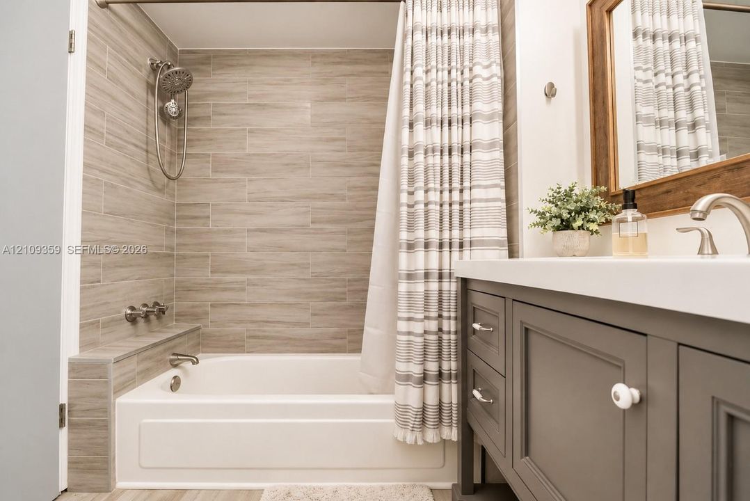 Bathroom featuring a built-in tub with neutral tile surround, multi-function shower head, matte finish vanity, and integrated solid surface countertop with a curved faucet