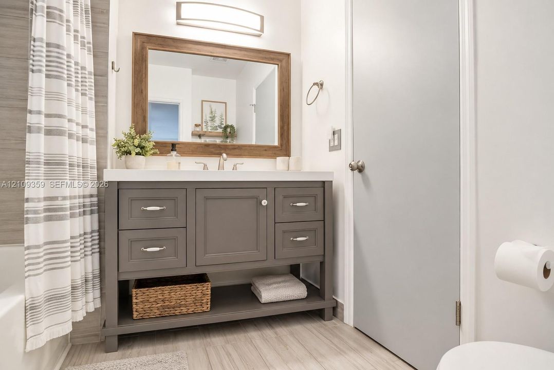 Grey vanity featuring a white countertop, under-mount sink, integrated lower shelving, and a large wood-framed mirror with an overhead light fixture