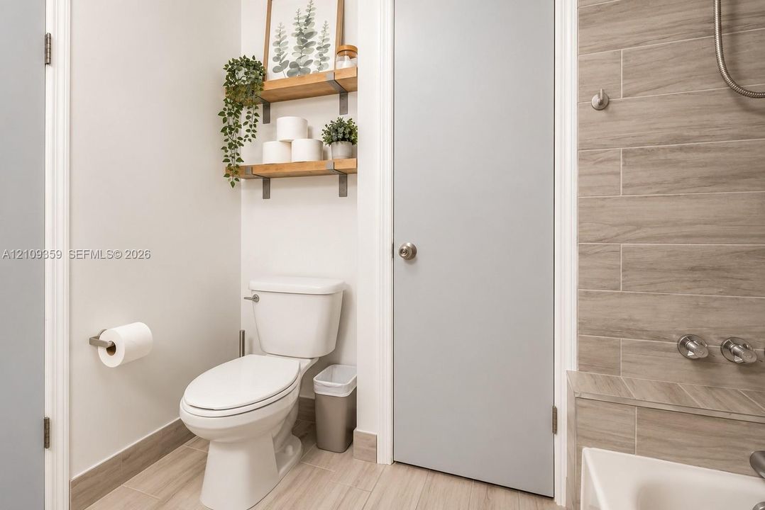 Bathroom featuring wood-finish floor tiling, wall-mounted floating shelves with metal brackets, a two-piece toilet, and tile-surround tub area