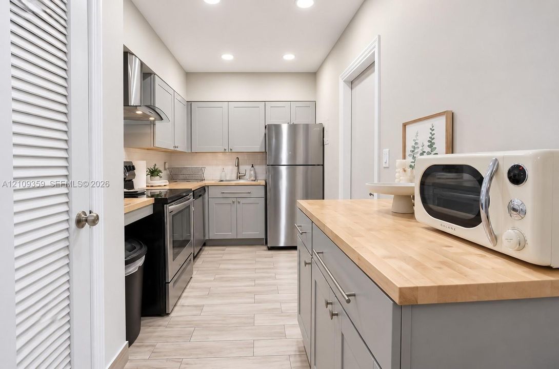 Kitchen featuring grey cabinetry, wood-finish countertops, stainless steel appliances, and wood-finish tile flooring