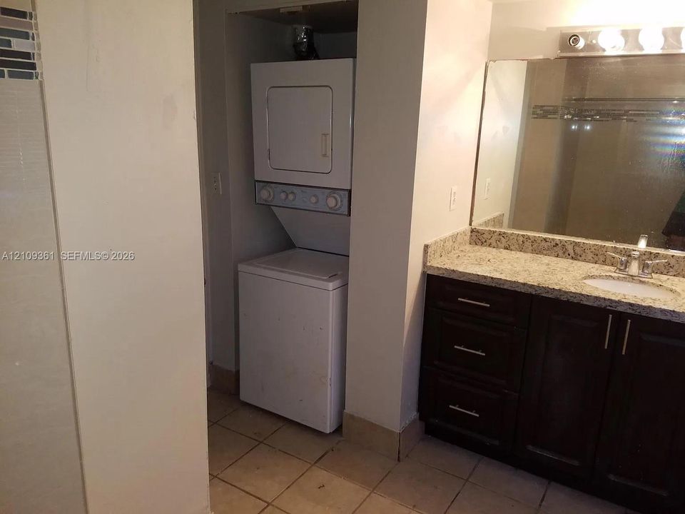 Stacked washer and dryer, vanity featuring stone-composite countertop, undermount sink, dark-finish cabinetry with metallic hardware, and full-width mirror