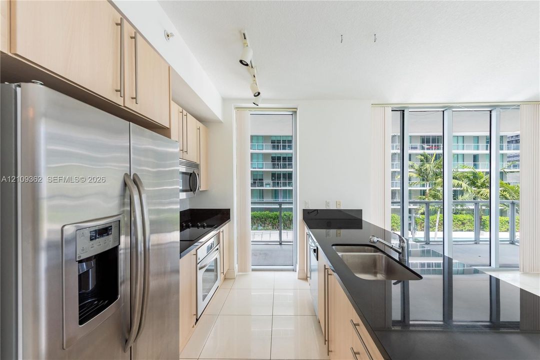 Kitchen featuring light wood-finish cabinetry, black stone countertops, stainless steel appliances, tile flooring, and floor-to-ceiling windows