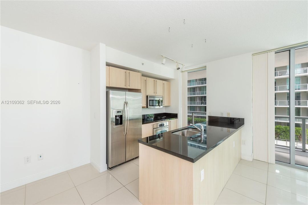 Kitchen featuring light wood-finish cabinetry, dark solid-surface countertops, stainless steel refrigerator, built-in microwave, and large-format tile flooring