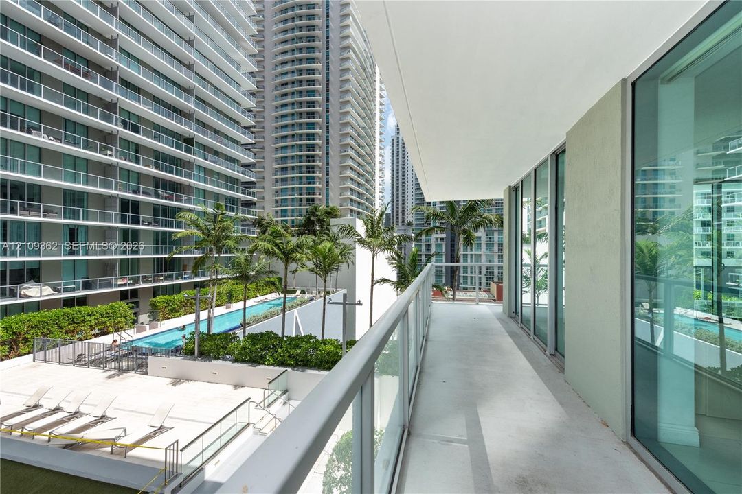 Covered balcony featuring a glass-panel railing, concrete flooring, and floor-to-ceiling glass wall