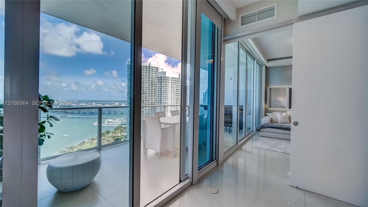 Floor-to-ceiling glass walls, expansive private balcony, polished tile flooring, and coastal water backdrop