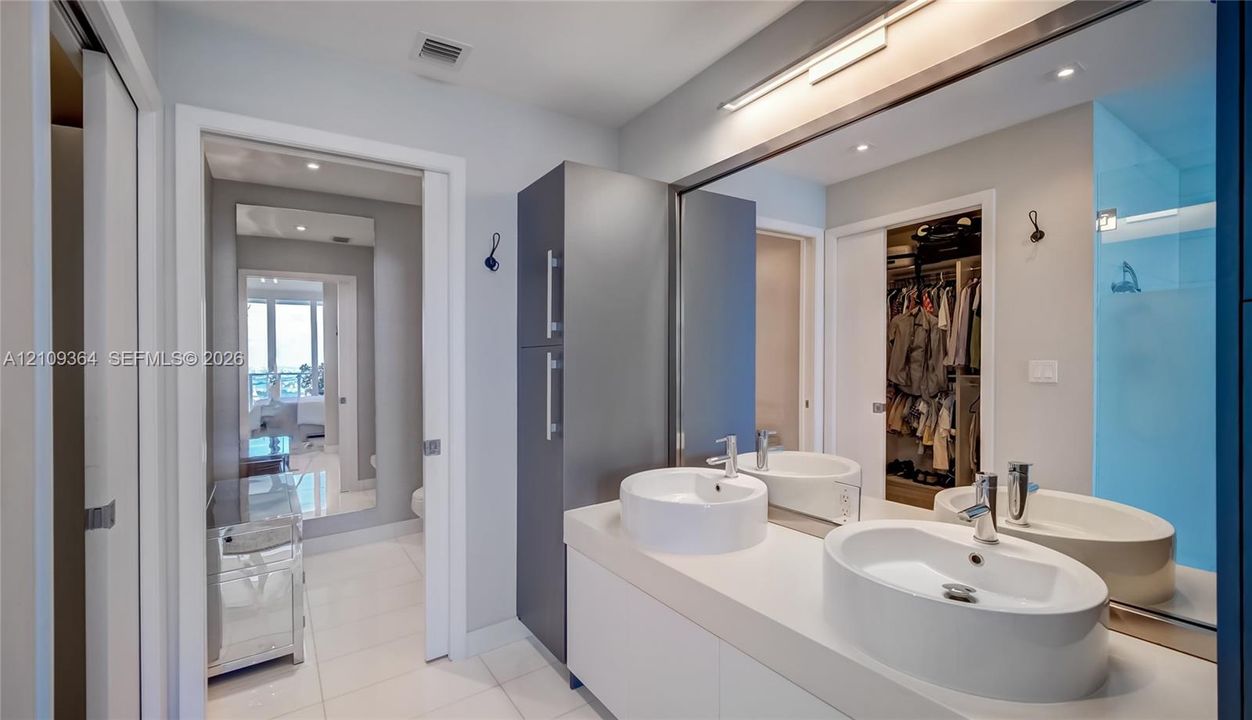 Dual white vessel sinks with chrome faucets, a flat-panel vanity, floor-to-ceiling cabinetry, wall-to-wall mirror, and tile flooring