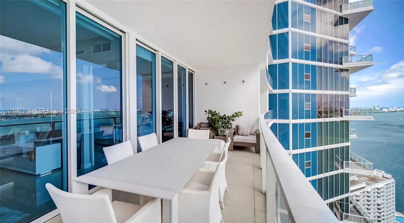 Expansive covered balcony featuring floor-to-ceiling glass paneling, tile flooring, glass railings, and wall-mounted exterior lighting