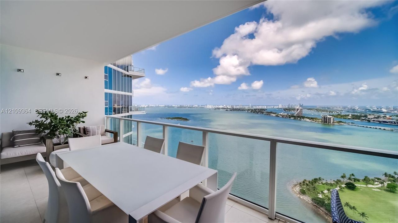 Covered balcony featuring oversized tile flooring, a glass panel railing, and wall-mounted lighting