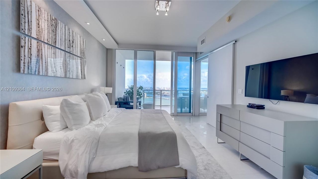 Floor-to-ceiling glass panel windows, polished tile flooring, recessed ceiling lighting, and sliding glass door access to a private balcony.
