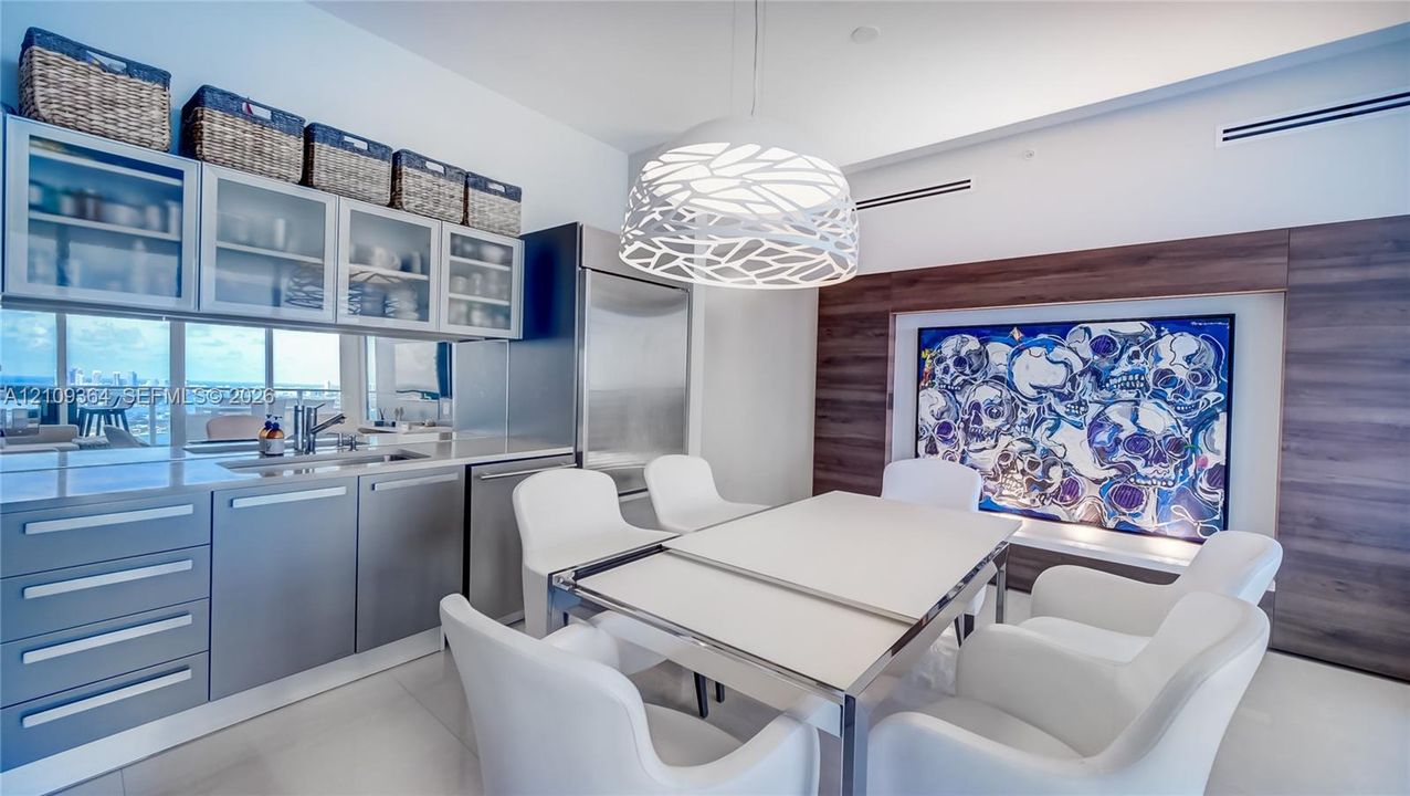 Kitchen featuring flat-panel cabinetry, glass-front upper cabinets, stainless steel appliances, a decorative pendant light fixture, and wood-finish wall paneling, Art piece not part of furnishings.