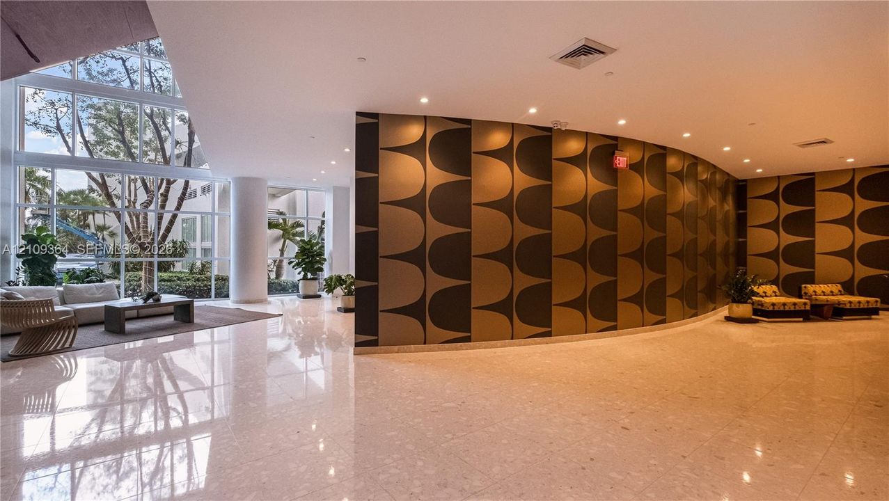 Expansive lobby featuring floor-to-ceiling windows, polished stone flooring, recessed lighting, and a curved architectural feature wall with patterned paneling where on-site management office is.