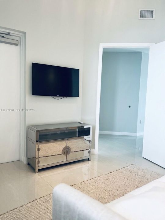 Mounted tv with mirror chest for the 2nd bedroom featuring neutral-toned walls, high-gloss tile flooring, and solid-core doors. One interior and the left is accessible to exterior.