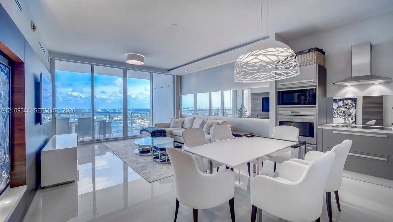 Open-concept interior featuring floor-to-ceiling glass sliding doors, high-gloss tile flooring, stainless steel built-in double wall ovens, and custom matte-finish cabinetry