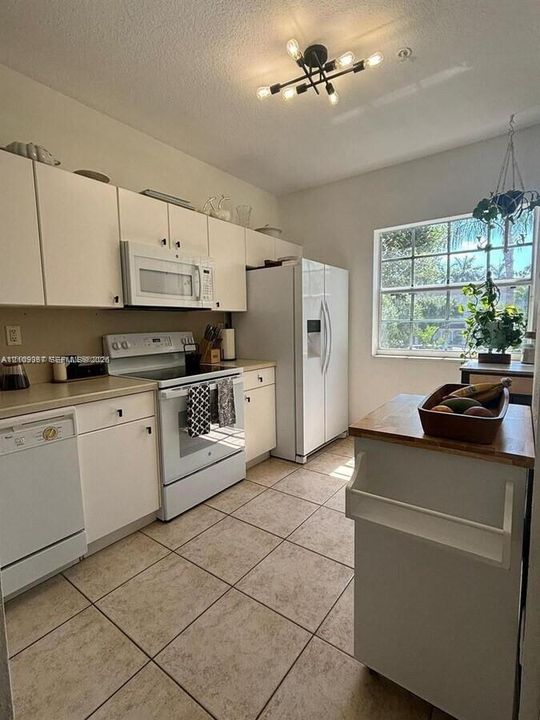 Kitchen featuring white cabinetry, ceramic tile flooring, a geometric multi-light fixture, and a large window