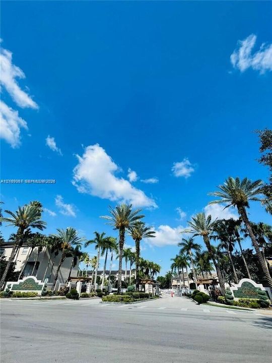 Gated entrance featuring decorative stone signage, established palm tree landscaping, and paved roadway
