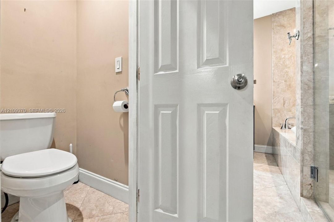 Bathroom featuring stone tile flooring, a glass-enclosed shower, a built-in bathtub with a stone tile surround, and a white toilet
