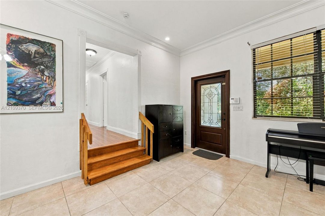 Entryway featuring tile flooring, a dark-stained wood front door with a decorative glass insert, crown molding, and wood-finish steps
