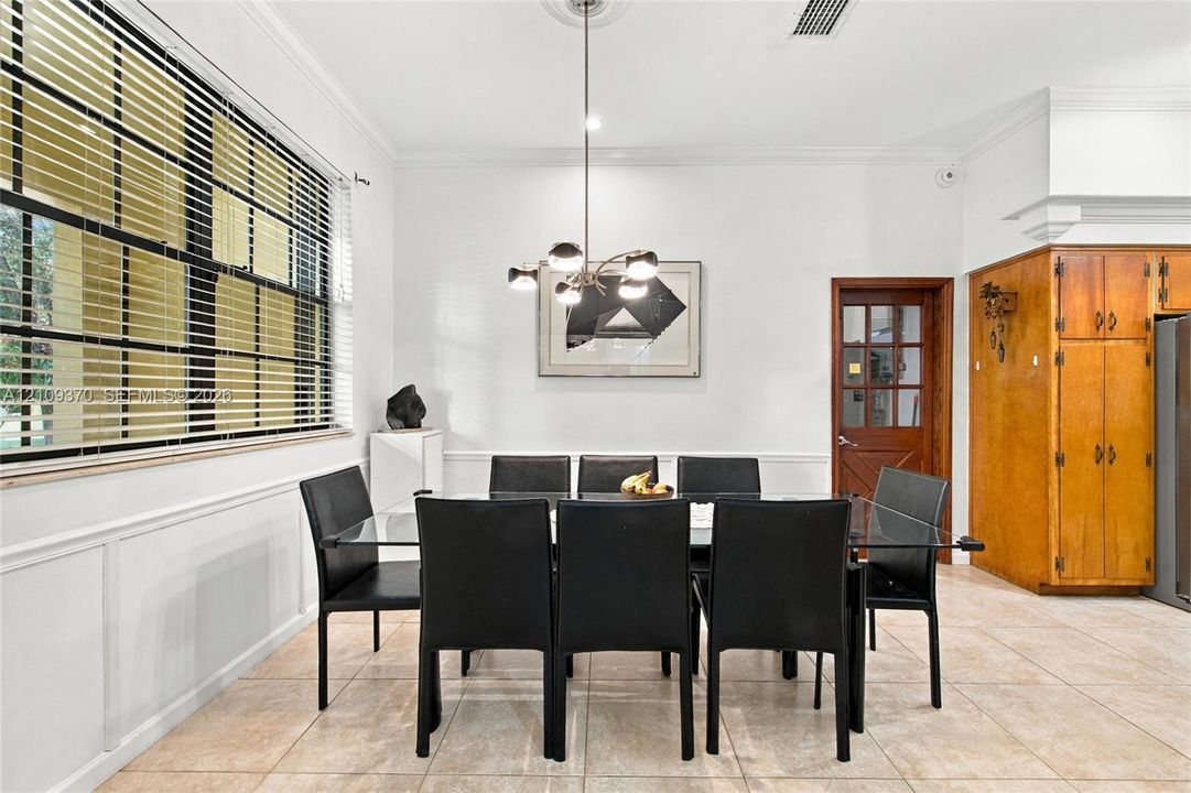 Dining area featuring tile flooring, wainscoting, a multi-light chandelier with a ceiling medallion, and custom cabinetry with wood-finish doors