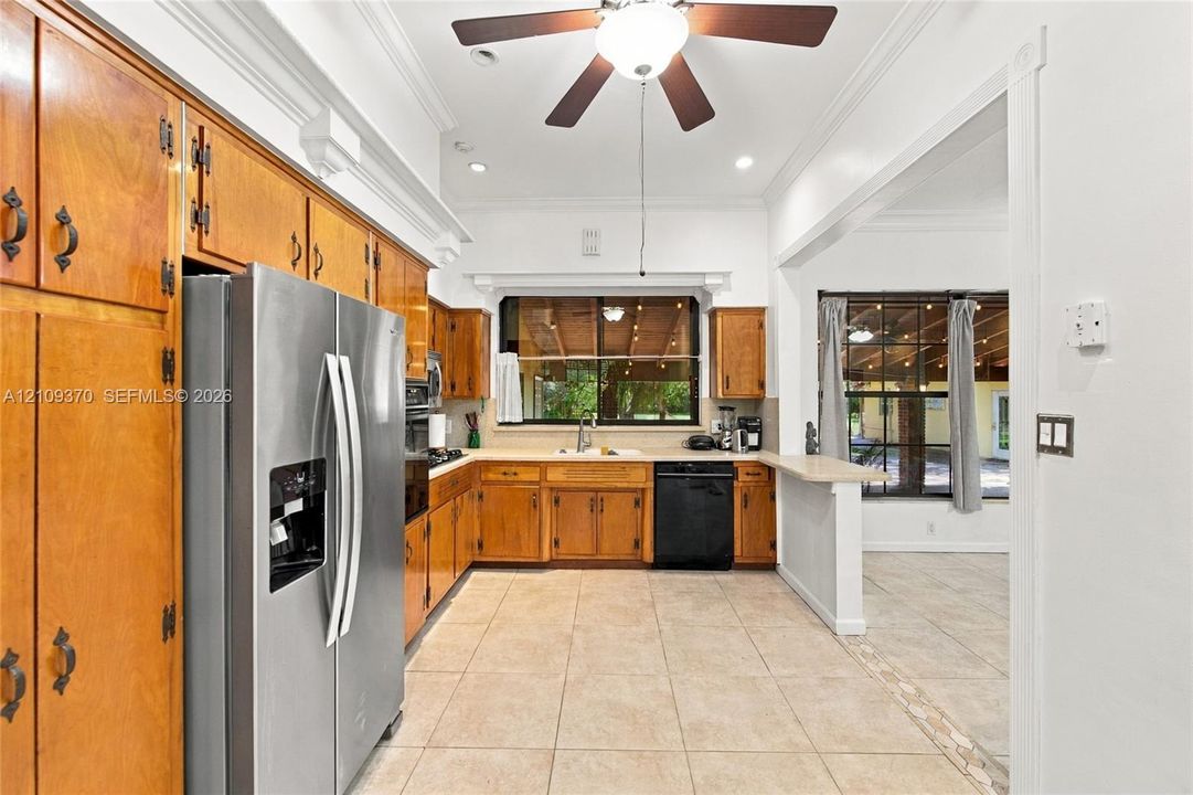 Kitchen featuring wood cabinetry, stainless steel appliances, tile flooring, crown molding, and a ceiling fan