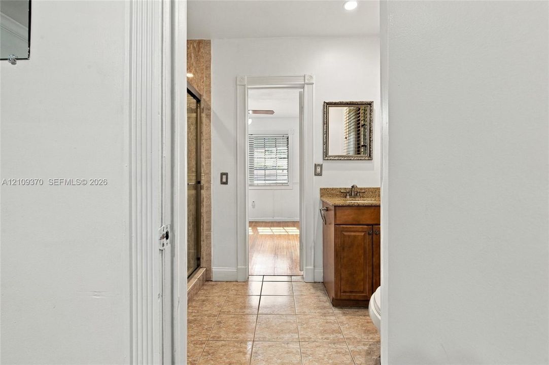Bathroom featuring tile flooring, a wood-finish vanity with a stone-top counter, a framed wall mirror, and a shower with glass doors and tile surround