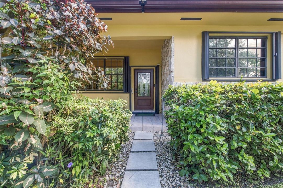 Exterior entry featuring a paved stone walkway, natural stone facade detailing, multi-pane windows with shutters, and a wood-panel door with a glass insert