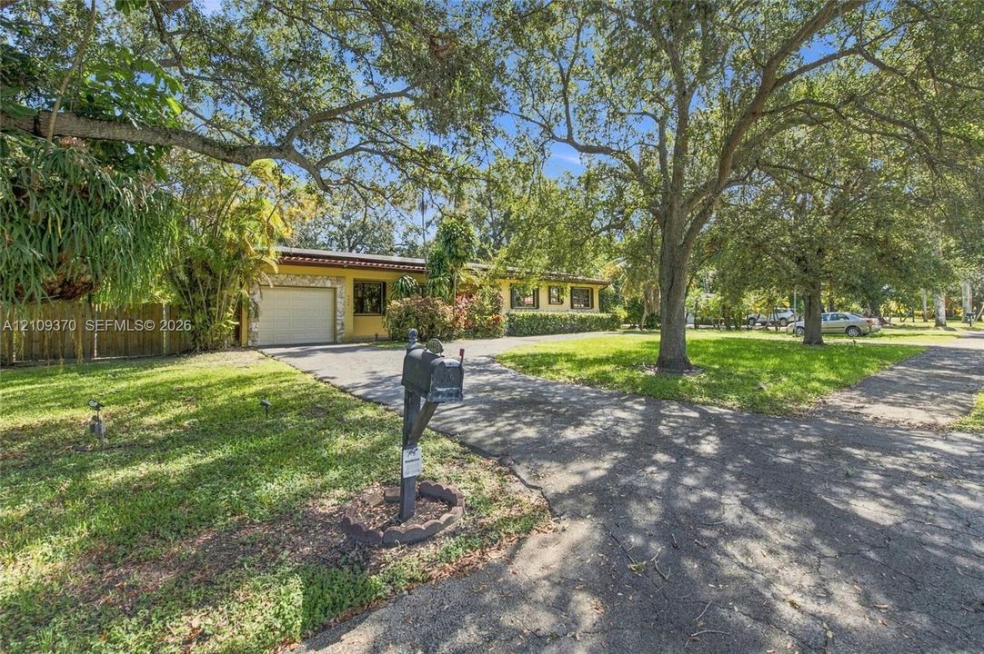 Single-story exterior featuring stone masonry accents, an attached garage, and mature trees on a sprawling lawn