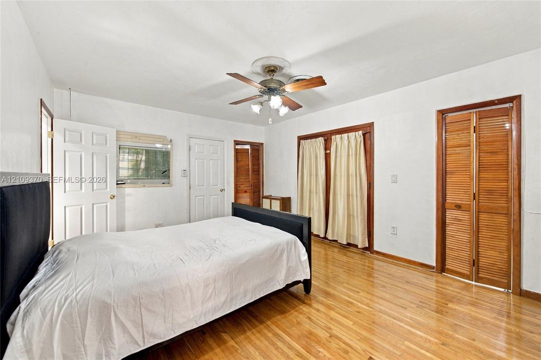 Wood-finish flooring, central ceiling fan with integrated lighting, and multiple wood-slat closet doors