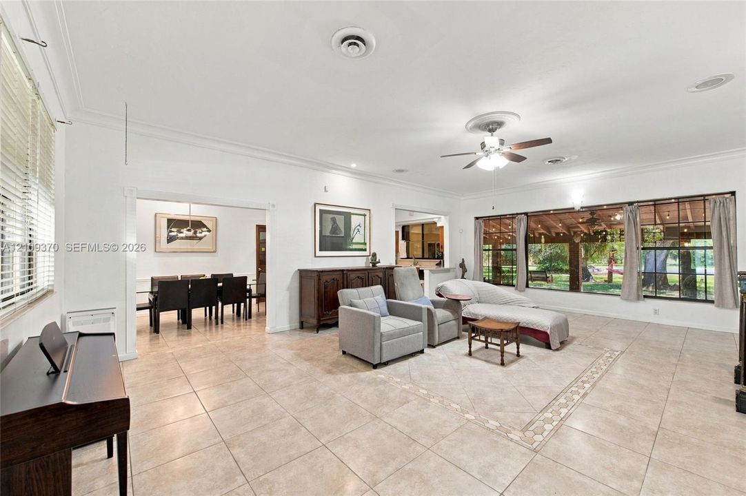 Open-concept living space featuring large-format tile flooring, crown molding, a central ceiling fan with integrated lighting, and expansive floor-to-ceiling windows