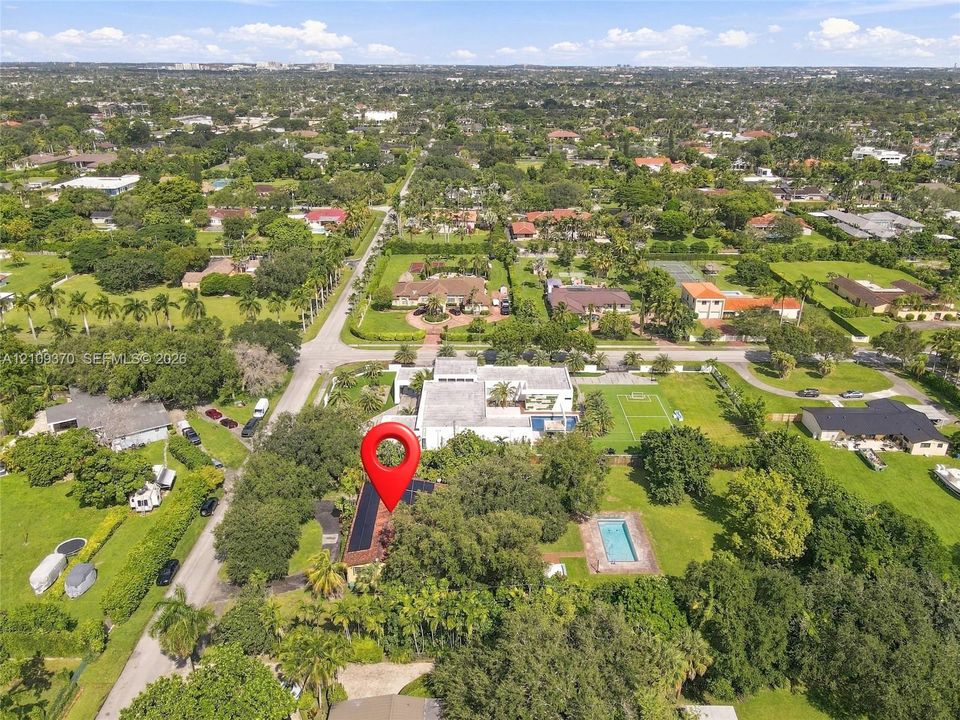 Aerial perspective of expansive residential lot featuring an in-ground swimming pool, solar panel array, and mature tree canopy