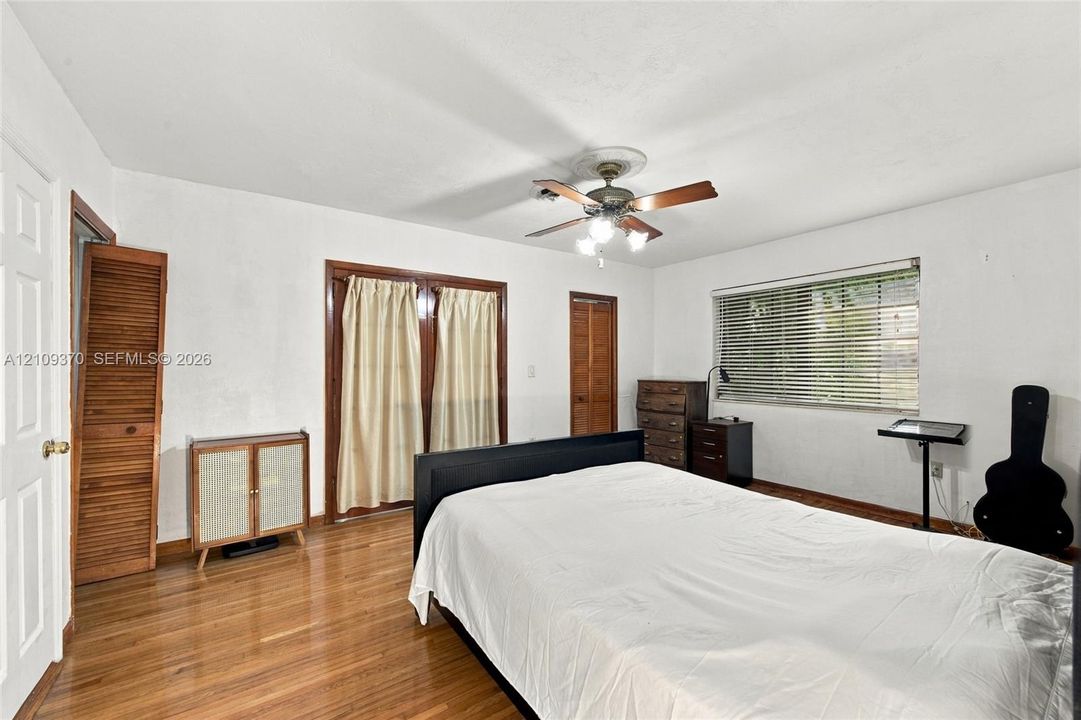 Room featuring wood-finish flooring, a ceiling fan with integrated lighting, glass-paneled double doors, and wood-finish louvered closet doors