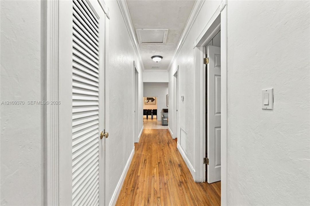 Hallway featuring wood-finish flooring, louvered closet doors, crown molding, and a recessed ceiling light fixture