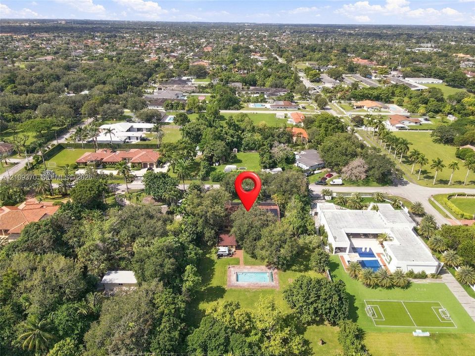 Aerial perspective of a property featuring an in-ground swimming pool, brick paver patio, expansive grounds, and mature tree canopy