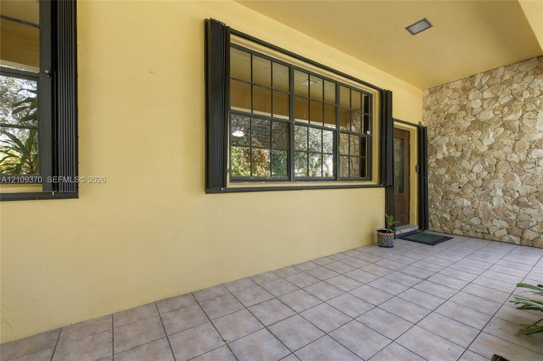 Covered patio featuring large-format tile flooring, a natural stone accent wall, grid-pane windows with metal frames, and an integrated ceiling light
