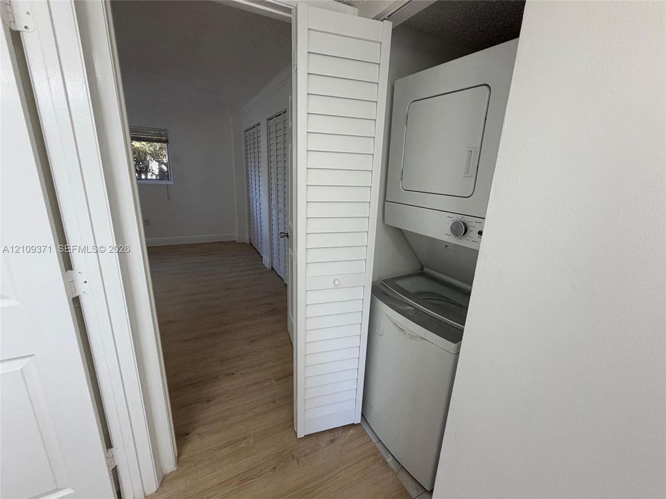 Stacked laundry unit enclosed by white louvered doors, featuring wood-finish flooring and paneled interior doors