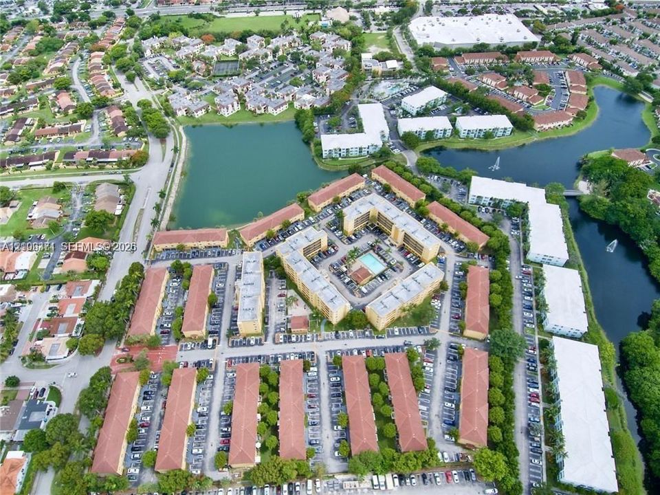 Aerial perspective of a multi-unit residential community featuring sprawling water features, mature landscaping, designated surface parking, and a centralized swimming pool