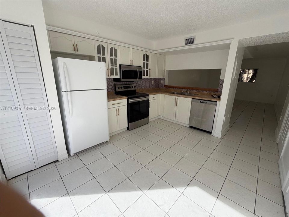 Kitchen featuring white cabinetry with glass-panel upper doors, stainless steel appliances, patterned backsplash, and tile flooring